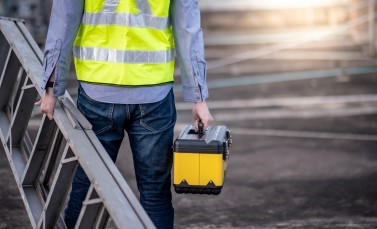 Man met ladder, geel hesje en gereedschapskist